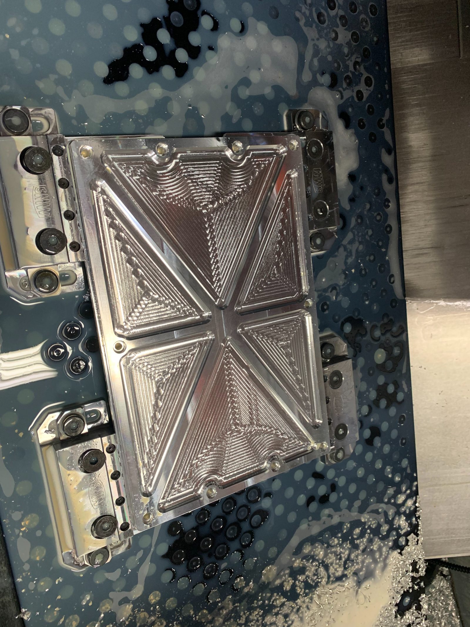 Decorative battery faceplate being CNC-machined - aluminum panel with diamond pattern geometry in machine with coolant
